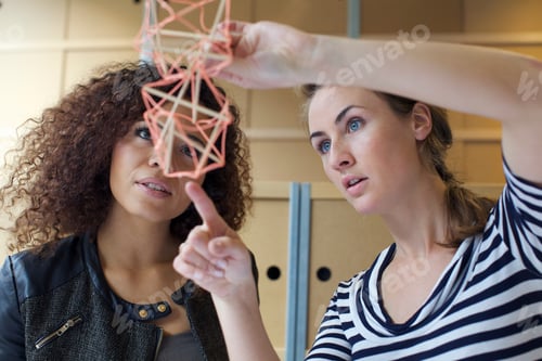 Preview: Two young female designers looking at handmade model in creative office