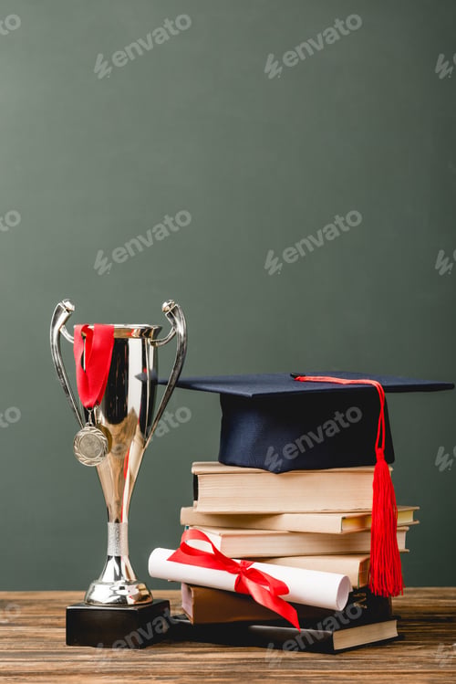 Preview: books, diploma, academic cap, trophy cup and medal on wooden surface isolated on grey