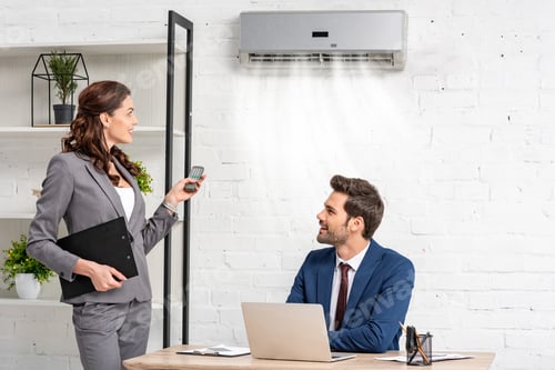 Preview: smiling businesswoman holding remote control while standing near handsome manager sitting at
