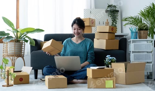 Preview: Happy young asian woman startup small business freelance holding parcel box and computer laptop and