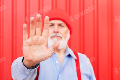 Preview: Closeup image of a elderly man outstretched hand and showing stop hand sign on red background