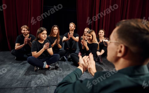 Preview: Sitting on the floor. Group of actors in dark colored clothes on rehearsal in the theater