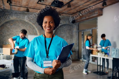 Preview: Happy black woman working as volunteer at donation center and looking at camera.