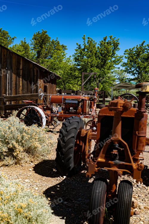 Preview: Vertical shot of a tractor in a sunny farm with trees and a barn in the background