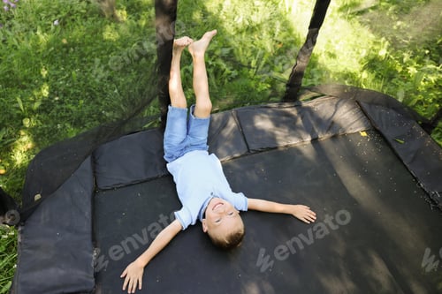 Preview: Happy little boy lying on black trampoline outdoors, above view