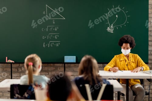Preview: African American teacher wearing face mask while examining students tests during a class.