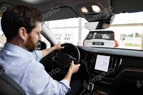 Preview: Businessman inside car dealership showroom test driving vehicle