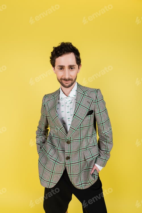Preview: Stylish man in shirt and checkered jacket posing with hands in pockets isolated on yellow