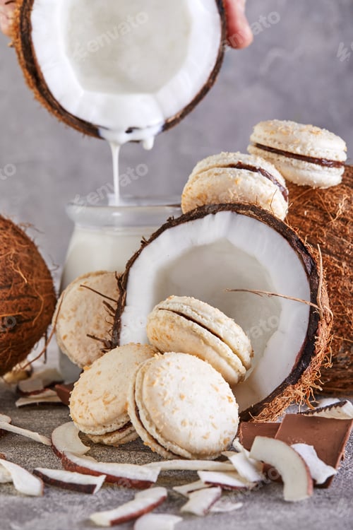 Preview: Coconut macarons with chocolate and coconut flakes on a table with a coconut in the background