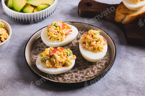 Preview: Spicy eggs stuffed with yolk, avocado and tomato on a plate on the table