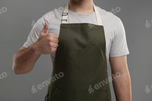 Preview: Man in kitchen apron showing thumb up on grey background, closeup. Mockup for design