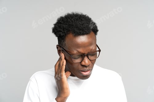 Preview: Black man frowning, suffering from tinnitus, throbbing earache, tired of noise, touching painful ear