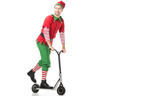 Preview: cheerful man in christmas elf costume riding push-cycle and looking away isolated on white