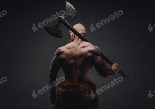 Preview: Rear view of healthy tattoed warrior in fur with axe on a dark background