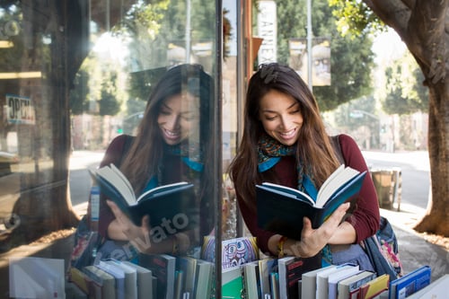Preview: Woman engrossed in a good book by a bookstore window, with her reflection creating a mirrored image