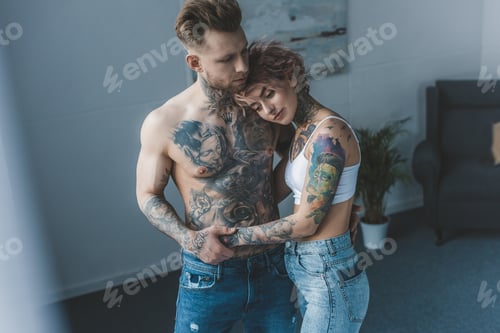 Preview: young tattooed stylish couple hugging in bedroom