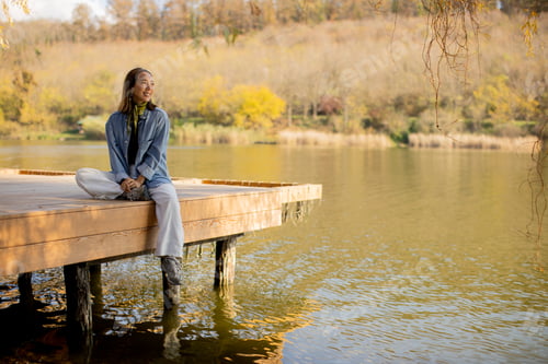 Preview: Relaxing on a wooden dock by the serene lake surrounded by autumn trees and golden hues