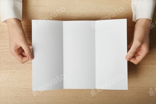 Preview: Woman holding blank brochure mock up on wooden table, top view