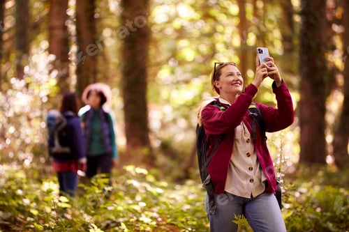Preview: Woman Taking Photo On Mobile Phone As Group Of Female Friends On Holiday Hike Through Woods Together