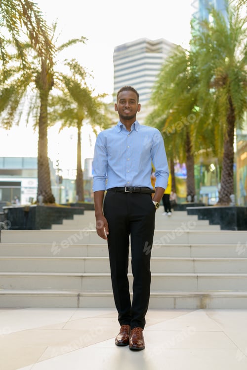 Preview: Full length shot of handsome black African businessman outdoors in city during summer smiling and