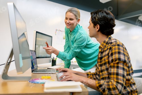 Preview: Side view of Caucasian male and female graphic designer discussing over computer at desk in office
