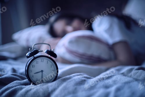 Preview: Young lady resting in her bed, midnight time shown on alarm clock, night dreams