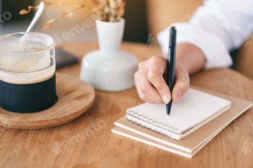 Preview: Closeup image of a woman writing on a blank notebook on wooden table