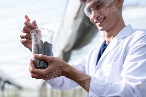 Preview: Glasses asian agricultural scientist man holding beaker testing on planting soils in greenhouse farm