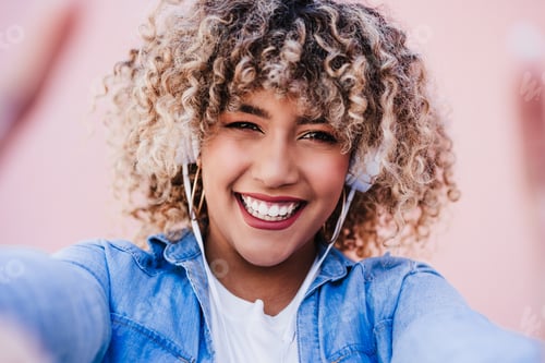 Preview: portrait of smiling hispanic woman with afro hair in city using mobile phone and headset. lifestyle