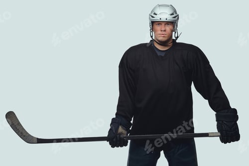 Preview: Hockey player wearing black protective uniform holds a hockey stick on a gray background.