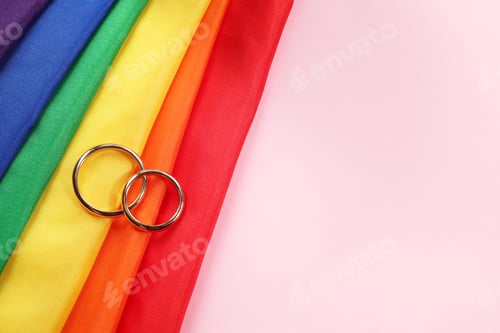 Preview: Rainbow LGBT flag and wedding rings on pink background, top view. Space for text