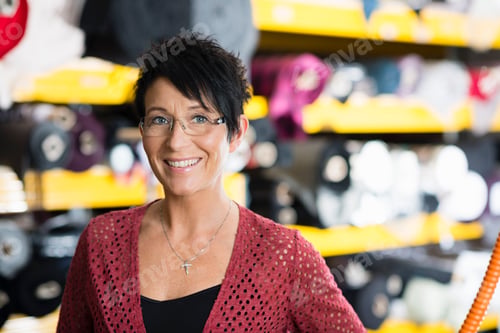 Preview: Portrait of mature seamstress in front of textile shelves in workshop