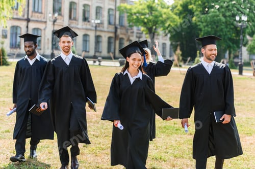 Preview: young graduated students in capes walking by university garden