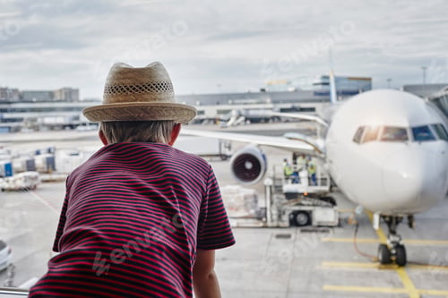 Preview: Boy wearing straw hat looking through window to airplane on the apron