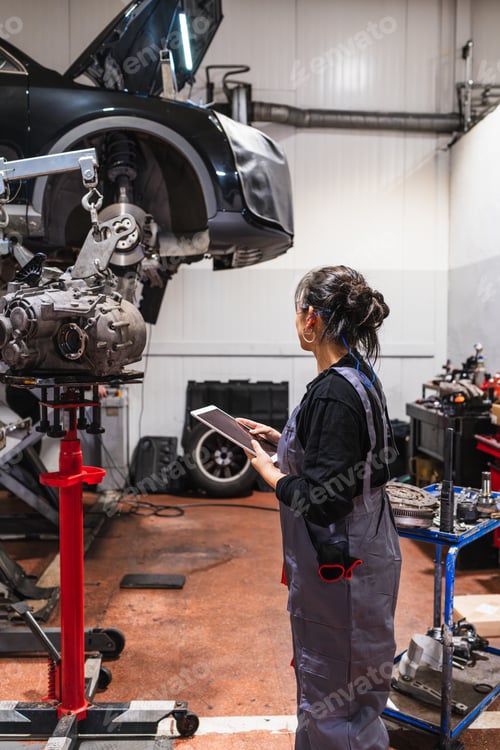 Preview: Female mechanic using digital tablet while examining car engine in repair shop