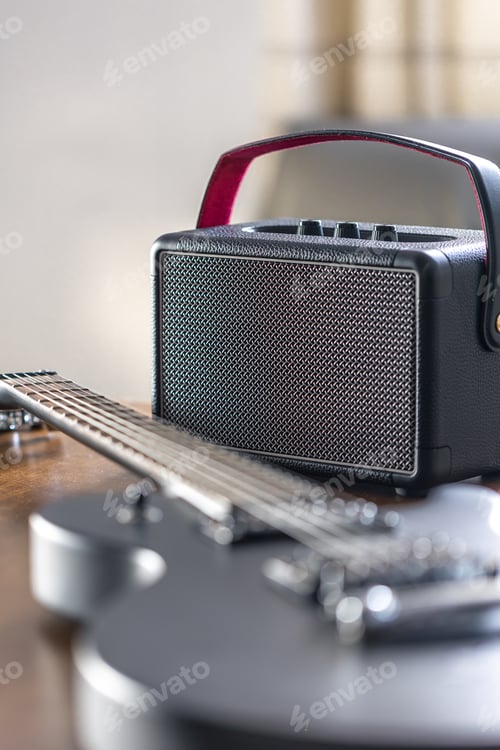 Preview: Black electric guitar and speaker on a wooden table.