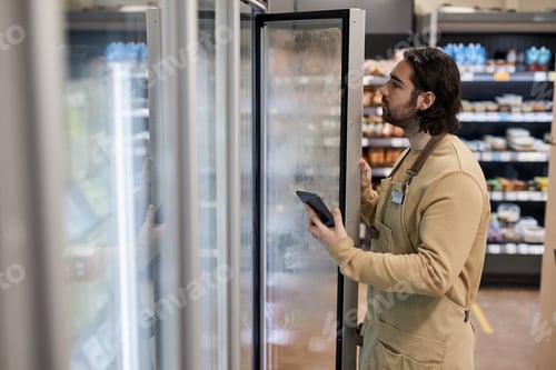 Preview: Male worker in supermarket inspecting freezer
