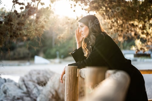 Preview: Sad woman dressed in black watching the sea with the sunset on the background