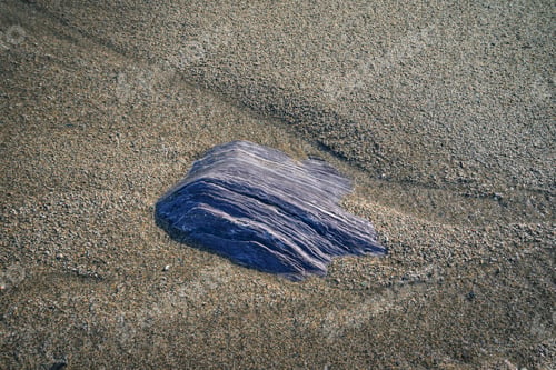 Preview: Fluorescent blue slate rock half buried in the sand of a beach
