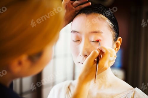 Preview: A modern geisha or maiko woman being prepared in traditional fashion, with white face makeup.