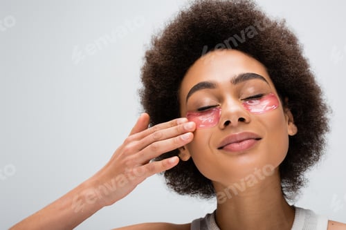 Preview: pleased african american woman with closed eyes touching hydrogel eye patch isolated on grey