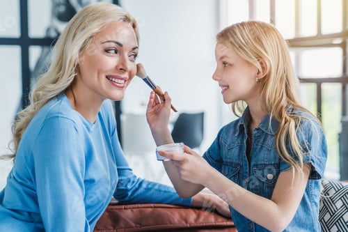 Preview: Cute little girl and her mother doing makeup while sitting on couch at home