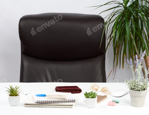 Preview: Empty brown leather armchair near a white table with a stack of notebooks