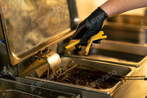 Preview: close-up in a professional kitchen a chef in black gloves puts French fries into a deep fryer