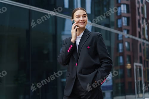 Preview: Creative manager woman in a black suit talking on a smartphone in an urban business area.