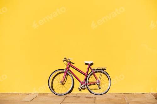 Preview: pink retro bike supported on a yellow wall