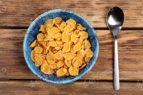 Preview: Bowl with healthy cornflakes and spoon on wooden table, top view