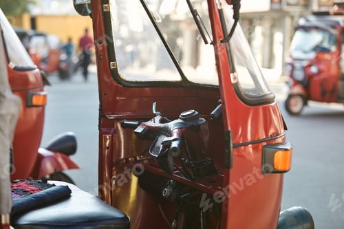 Preview: Red tuk tuk parked against busy street. Popular three wheeled motorcycle in Sri Lanka.