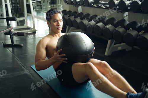 Preview: Asian handsome man working out his abdominal muscles by holding the bag twist left and right sitting
