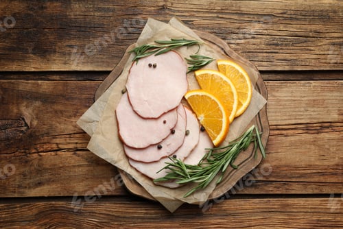 Preview: Delicious cut ham with rosemary, peppercorns and orange slices served on wooden table, top view